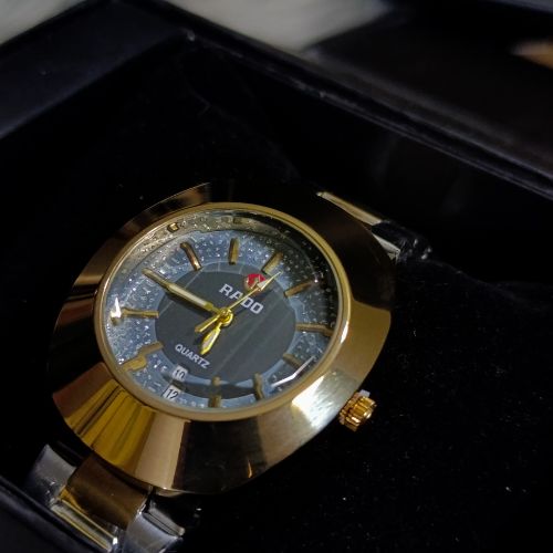 Stylish Rado DiaStar men’s watch in gold finish, black dial with clear markers, and stainless steel bracelet chain.